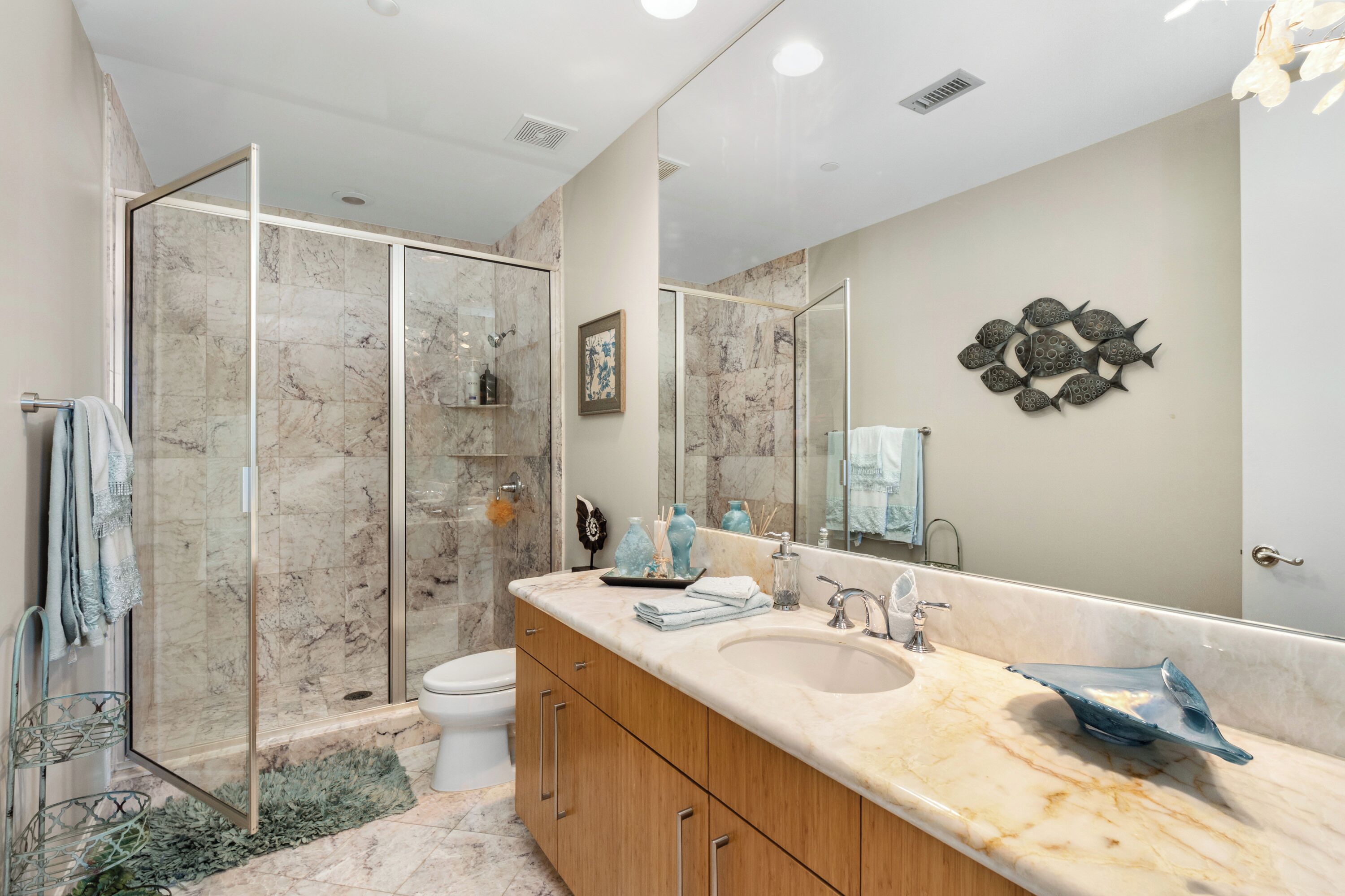 A modern bathroom with a glass-enclosed shower, a large mirror, and marble countertops.