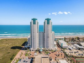 A high-rise hotel with a view of the ocean, featuring multiple balconies and a parking lot. - Beachfront Beauty with Amazing Views & Resort Pool (South Padre Island)