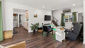 En moderne stue med et fladskærms-tv, en behagelig sofa, et skrivebord med en computer og en læderlænestol.