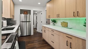 Et moderne køkken med træskabe, rustfrie hvidevarer og en backsplash oplyst af grønt lys.