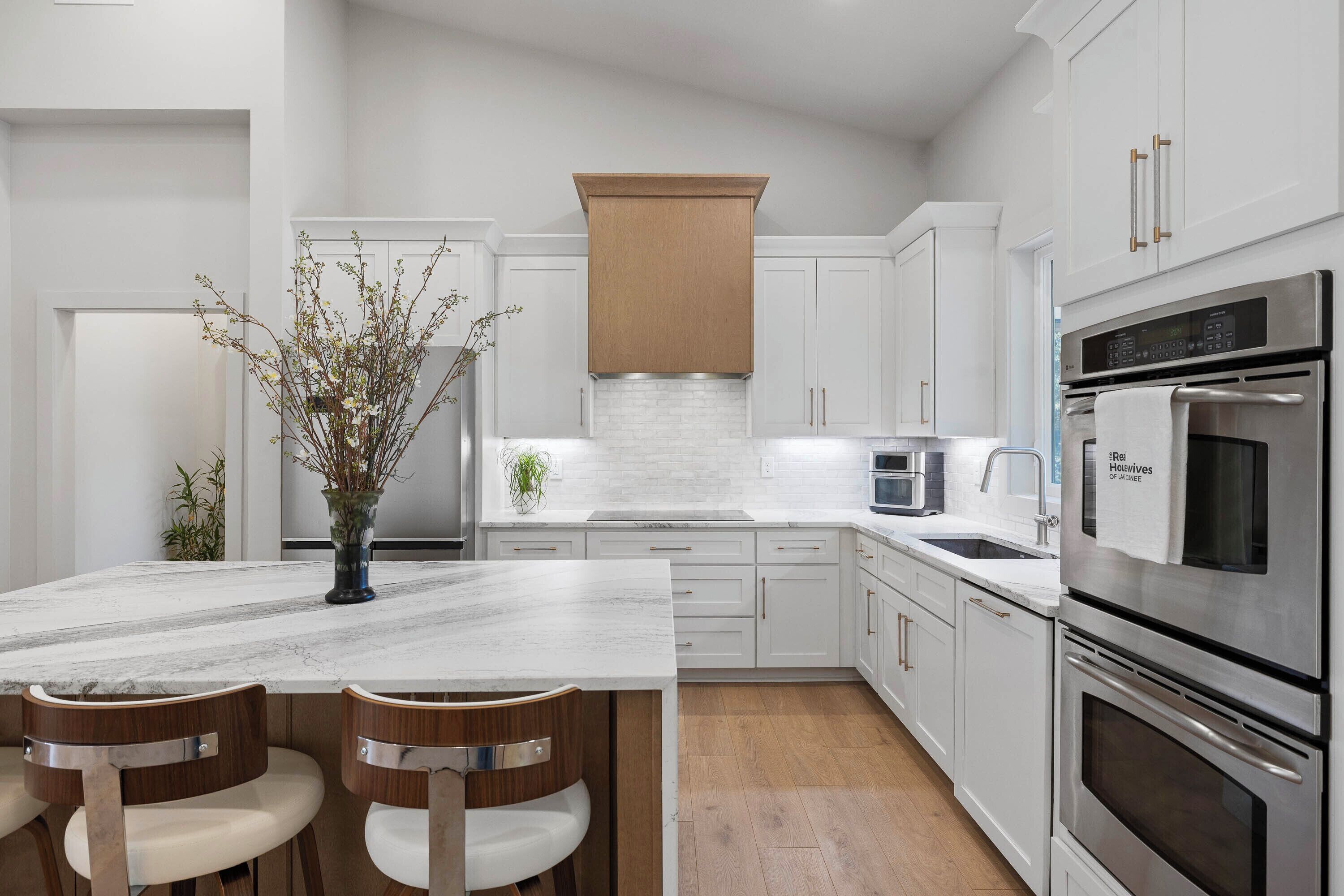 A modern kitchen with white cabinets, a marble countertop, and stainless steel appliances.