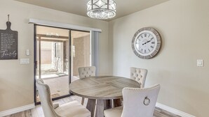 Een eetruimte met een ronde tafel, vier gestoffeerde stoelen, een wandklok en een kroonluchter.