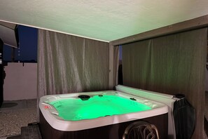 Ein Whirlpool mit grüner Beleuchtung, umgeben von Vorhängen und einer hölzernen Sitzbank.
