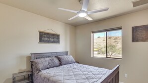 Een slaapkamer met een bed, nachtkastje, plafondventilator, raam en inspirerende wanddecoratie.