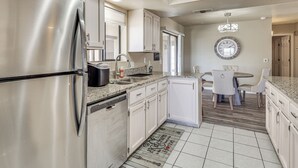 Een moderne keuken met roestvrijstalen apparatuur, witte kasten en een eethoek met een ronde tafel en stoelen.