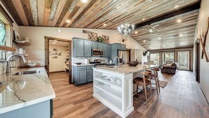 A spacious kitchen with wooden flooring, a central island, and grey cabinets. - Cossatot River Retreat: Home w/ Fire Pit & Grill (Gillham)