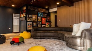 Ein modernes Wohnzimmer mit einer Eckcouch, bunten Poufs und einer Wand mit gerahmten Kunstwerken.