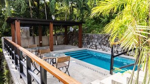 Ein Poolbereich mit Holzterrasse, Sitzgelegenheiten und einer Steinmauer.