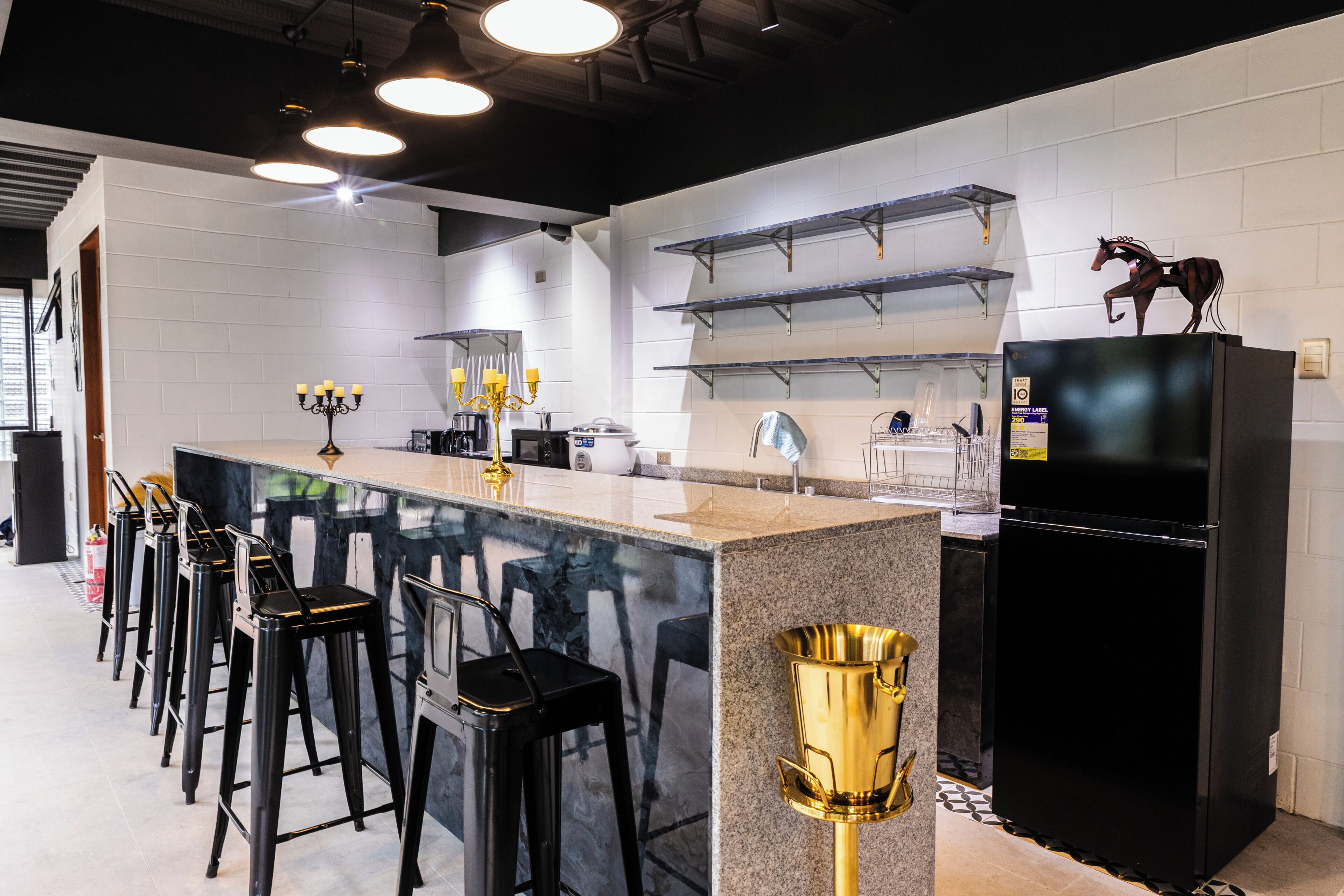 A modern kitchen with a marble island, black bar stools, a black refrigerator, and a gold decorative item.