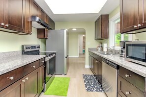 A modern kitchen with dark wood cabinets, stainless steel appliances, granite countertops, and a green rug. - Amazing 4-bedroom house with AC in enchanting Federal Way (Federal Way)
