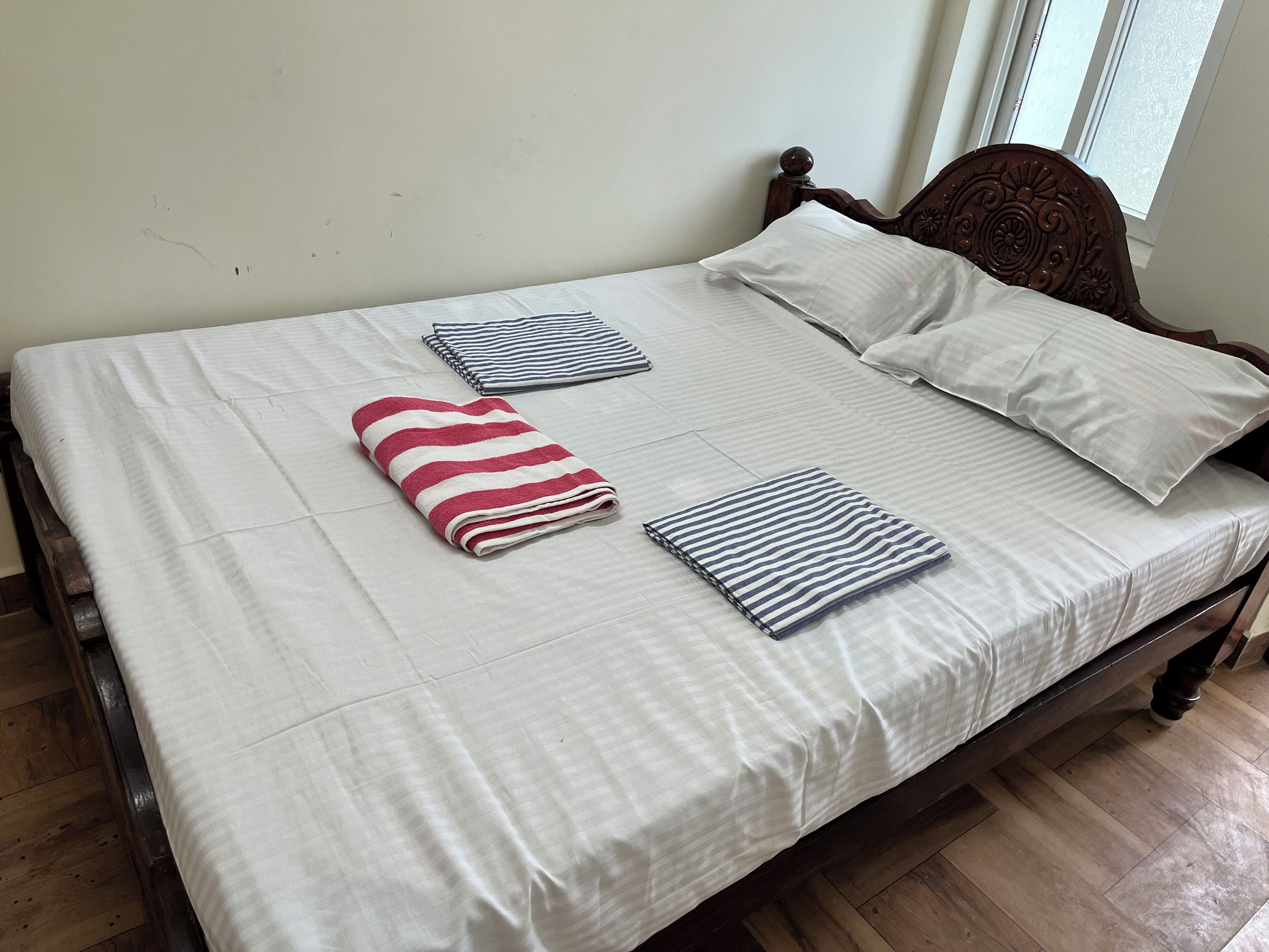 Een net opgemaakt bed met een witte spreidek, twee kussens en twee opgevouwen handdoeken.