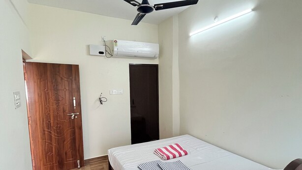Une chambre à coucher avec un lit, un ventilateur de plafond, un appareil de climatisation et une porte en bois.