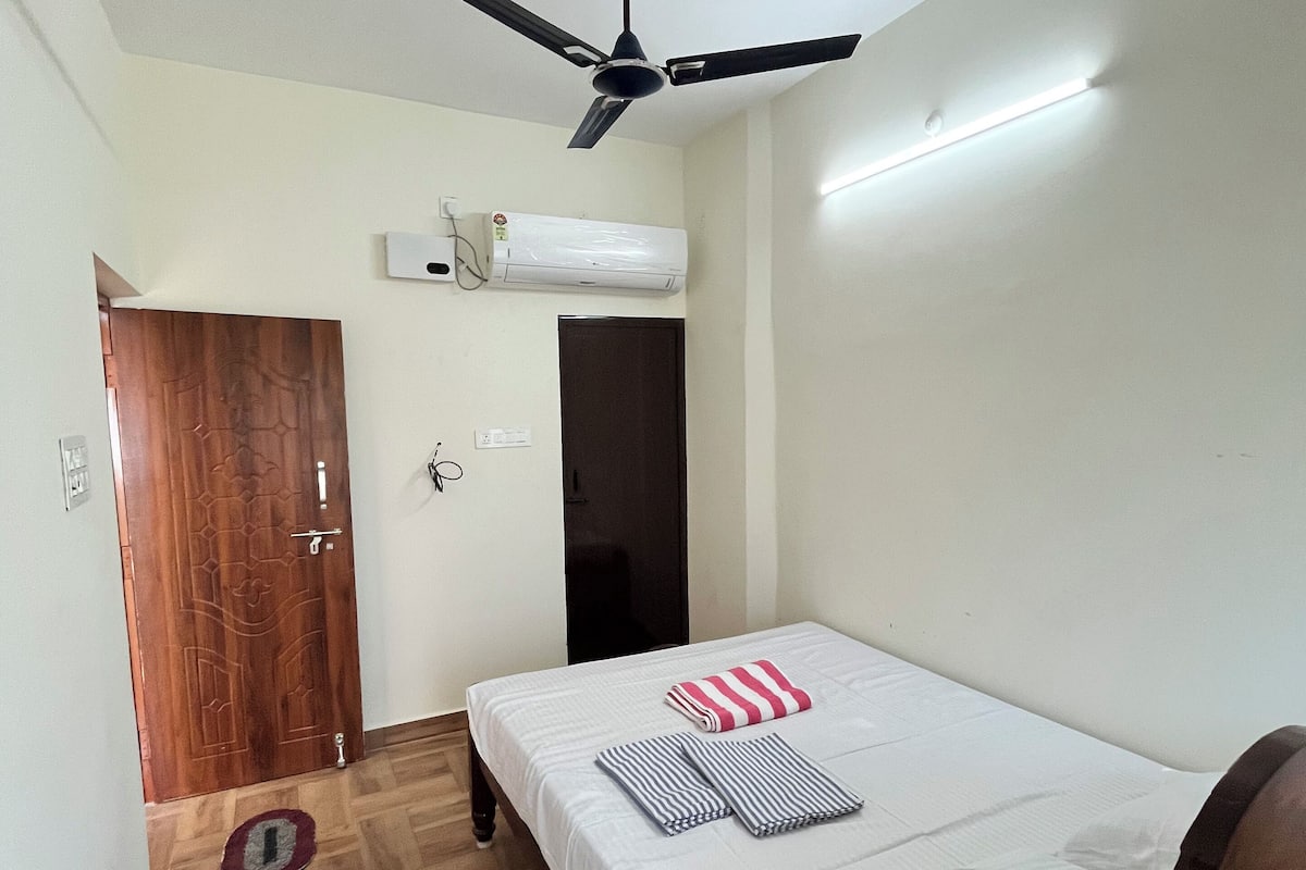Un dormitorio con cama, ventilador de techo, equipo de aire acondicionado y puerta de madera.