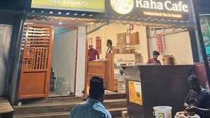 Un bâtiment avec une enseigne indiquant « Raha Rooms (chambres avec et sans climatisation) » et « Raha Cafe », proposant du thé et des collations de Vanyambadi.