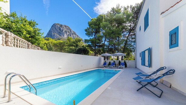 A swimming pool with a mountain view, lounge chairs, and a bottle of champagne. - Apartments with pool on the Makarska Riviera near the sea (Zaostrog)
