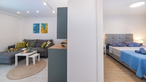 A modern apartment with a grey sofa, a small white table, and a bed with blue bedding. There are two wall art pieces above the sofa. - Apartments with pool on the Makarska Riviera near the sea (Zaostrog)