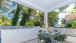 An outdoor patio with a table set for two, surrounded by greenery and a white fence. - Apartments with pool on the Makarska Riviera near the sea (Zaostrog)