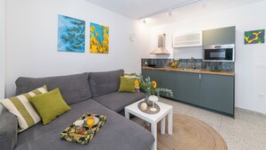 A modern living room with a grey sofa, a small white table, and a kitchen area with a microwave and stove. - Apartments with pool on the Makarska Riviera near the sea (Zaostrog)