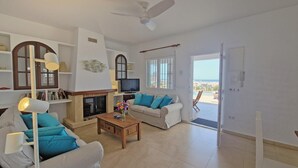 Una sala de estar con sofá, mesa de centro, televisión, estantería y chimenea.