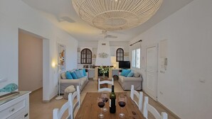 Un amplio salón con una mesa de comedor preparada para cuatro personas, un sofá, un televisor y un ventilador de techo.