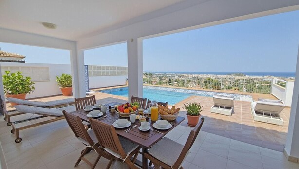 Un balcón con mesa lista para el desayuno, una piscina y vistas a la ciudad.