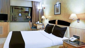 Habitación de hotel con una cama grande, un escritorio con lámpara, teléfono y ventana con cortinas.