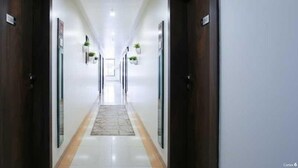 Un pasillo largo y estrecho con puertas a ambos lados, suelo de baldosas y pequeñas macetas en las paredes.