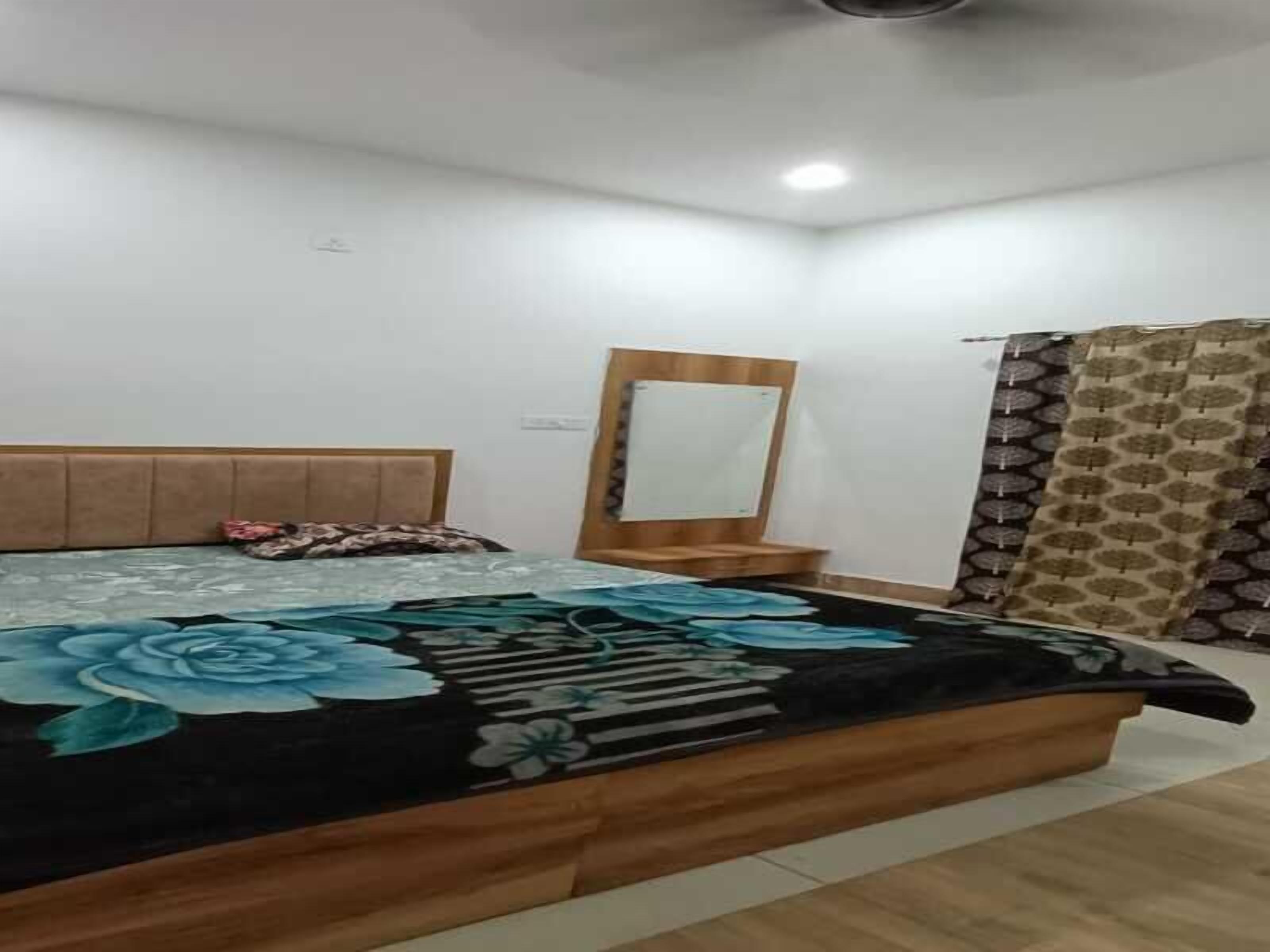 Een slaapkamer met een bed, een houten hoofdbord, een spiegel en een gordijn met een patroon.