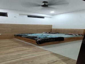 A bedroom with a bed, wooden paneling, a ceiling fan, and a small window. - Hotel Maa Karni Darbar (Bikaner)
