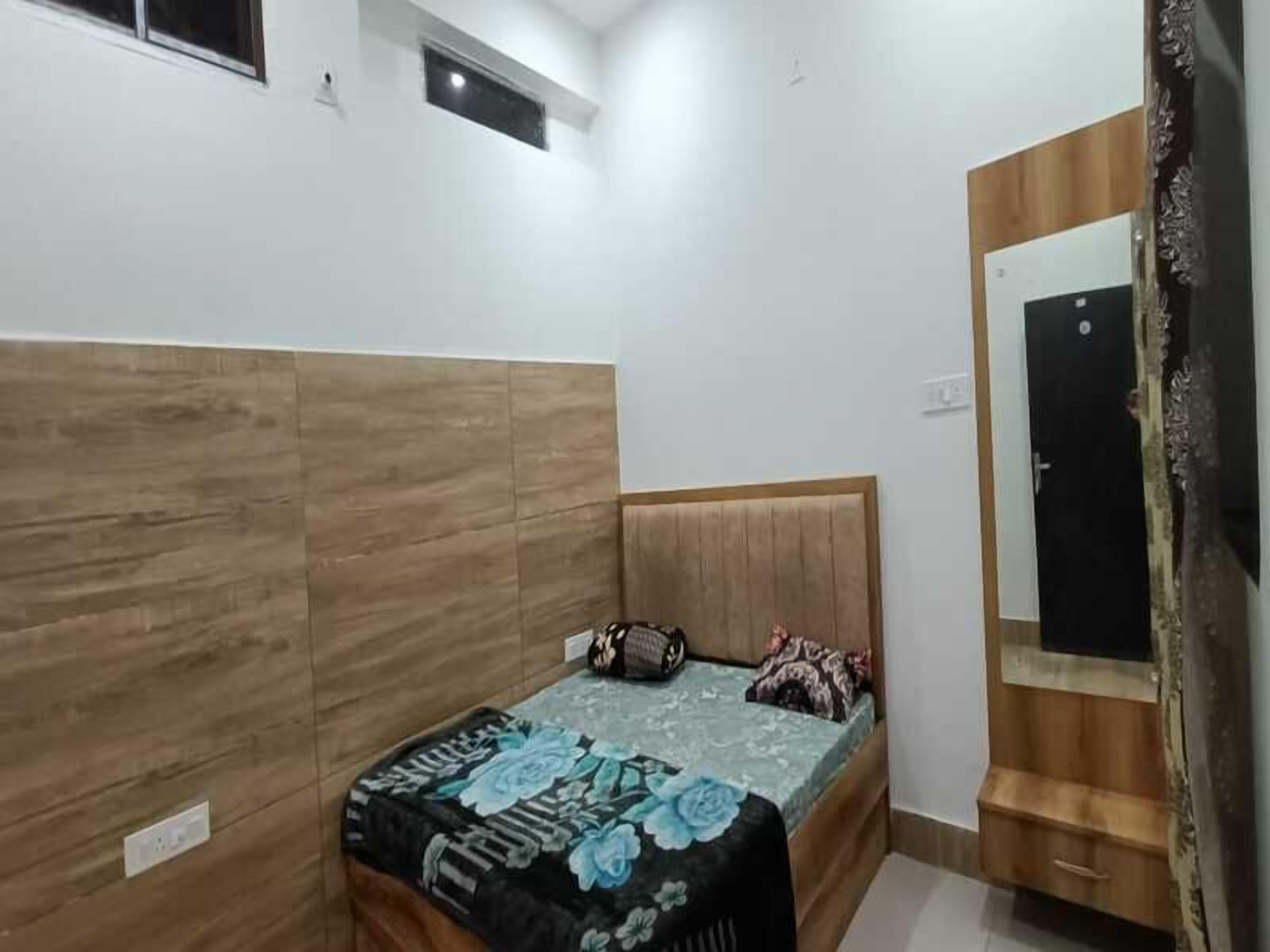 A bedroom with a wooden headboard, a bed with a floral bedspread, a bedside table, and a mirror.