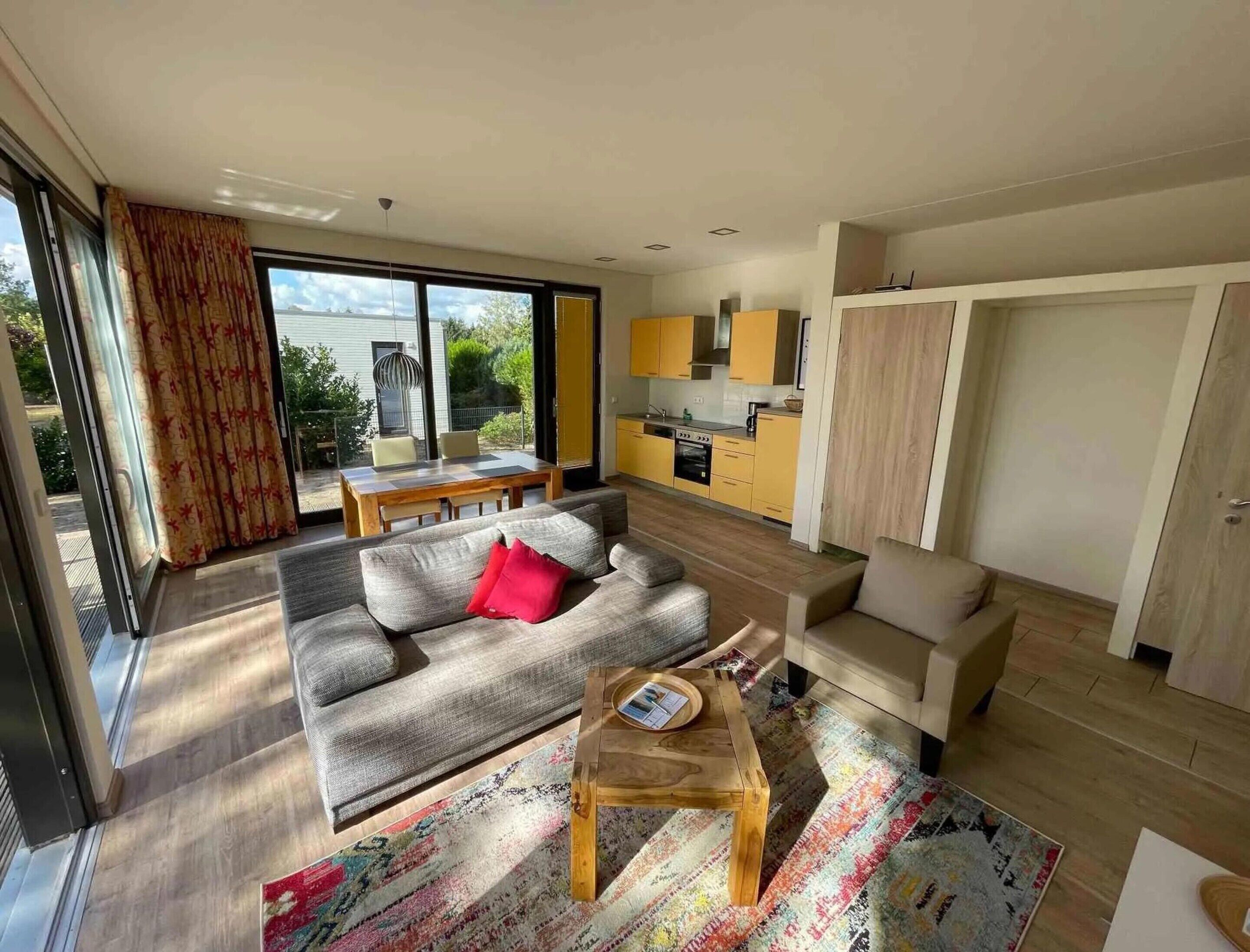 En moderne stue med sofa, sofabord og spiseområde med bord og stole. Der er et køkken med gule skabe og en skydedør.