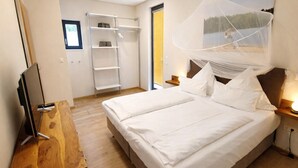 Un dormitorio con cama, mesitas de noche, televisor, armario y ventana.