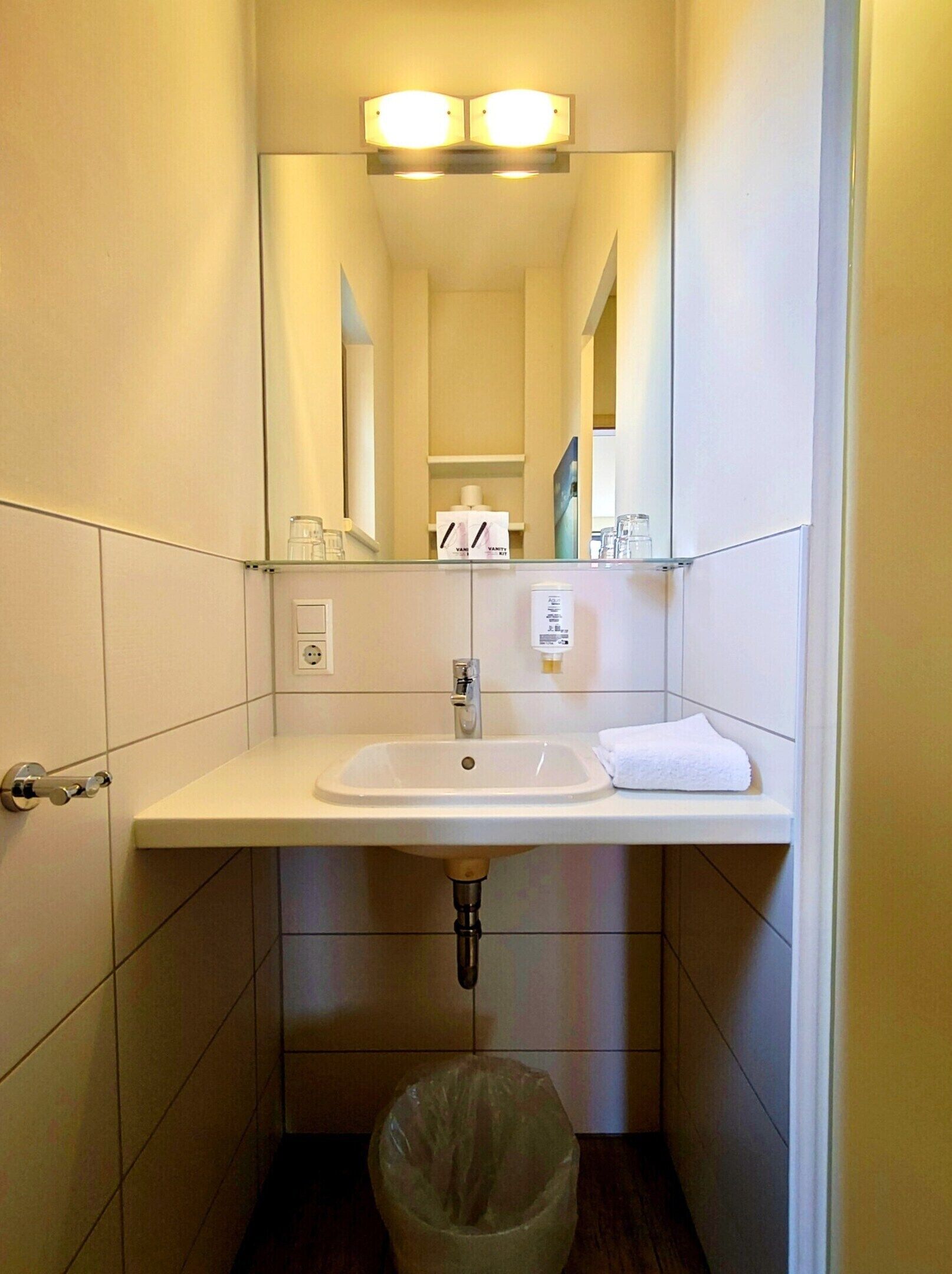 Une petite salle de bain avec un lavabo blanc, un miroir et une poubelle.
