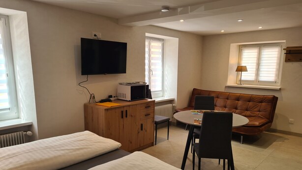 Ein Hotelzimmer mit einem Bett, einem Schreibtisch mit Computer, einem Fernseher, einem Sofa und einem Fenster.