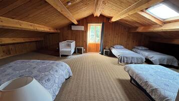 A cozy attic bedroom with wooden walls, a sloped ceiling, and a skylight. It includes two beds, a crib, and a small table.