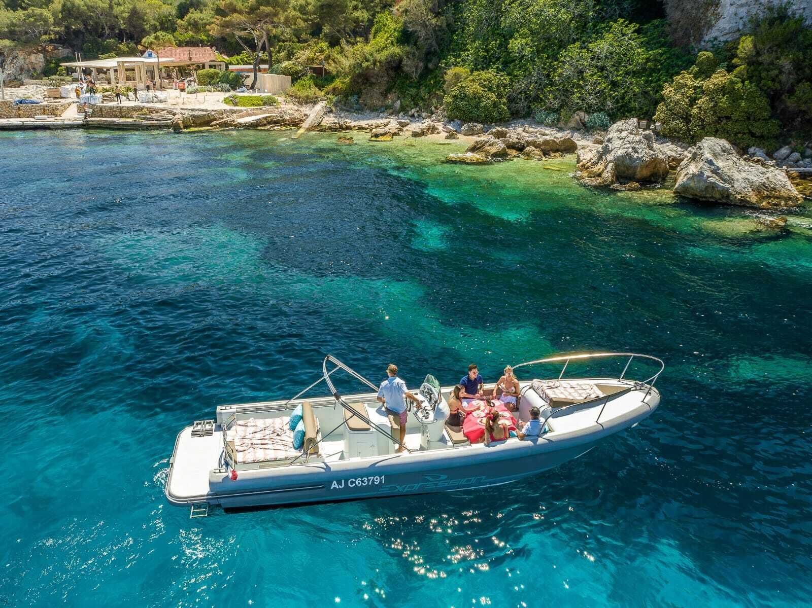 A boat with people on board, clear blue water, and a rocky shoreline with trees in the background.