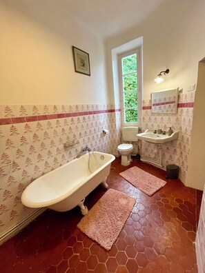 A bathroom with a bathtub, toilet, sink, and a window with a view of greenery.