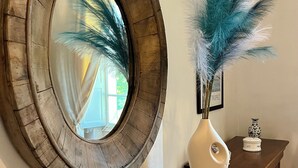 A mirror with a rustic frame, a vase with blue feathers, and a small white sculpture on a marble countertop.