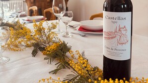 A dining table with a bottle of Castellas Agay wine, yellow flowers, and empty wine glasses.