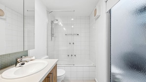 A modern bathroom with a large mirror, white tiles, a bathtub, and a toilet.