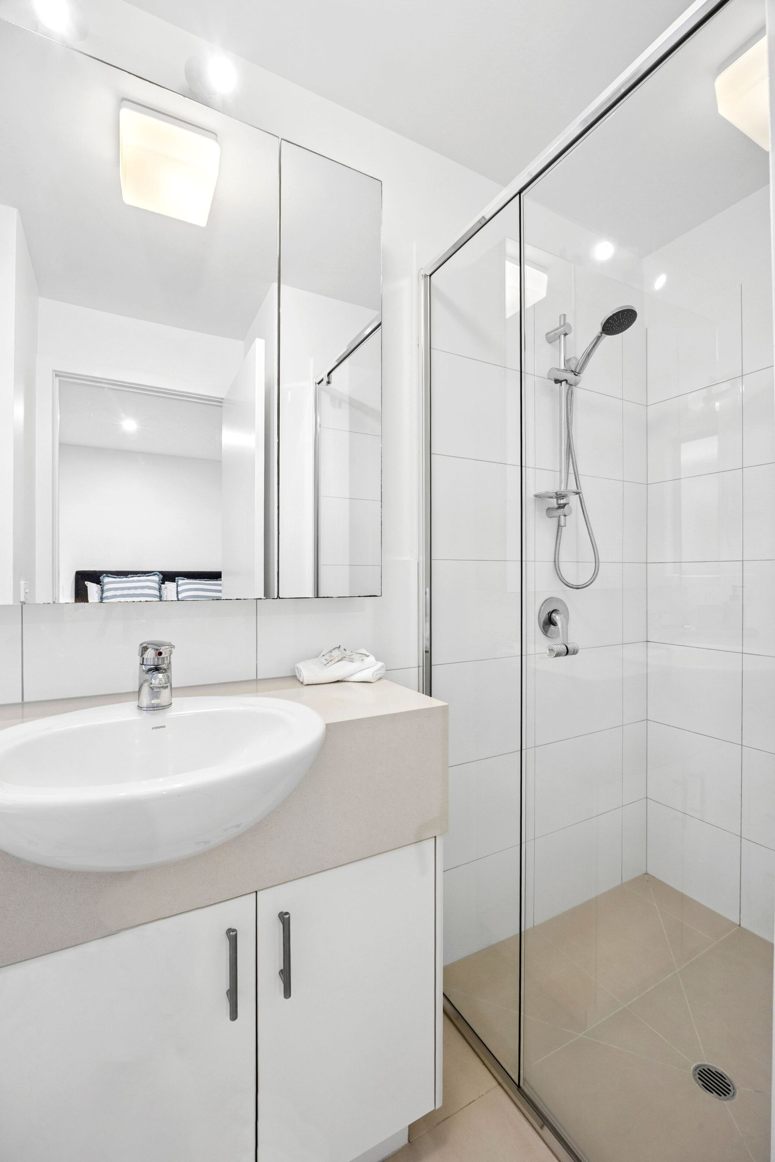 A modern bathroom with a glass-enclosed shower, a white sink, and a large mirror.