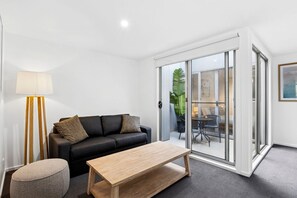 Ein modernes Wohnzimmer mit Sofa, Couchtisch, Lampe und einer Schiebeglastür, die zu einem Außenbereich führt.