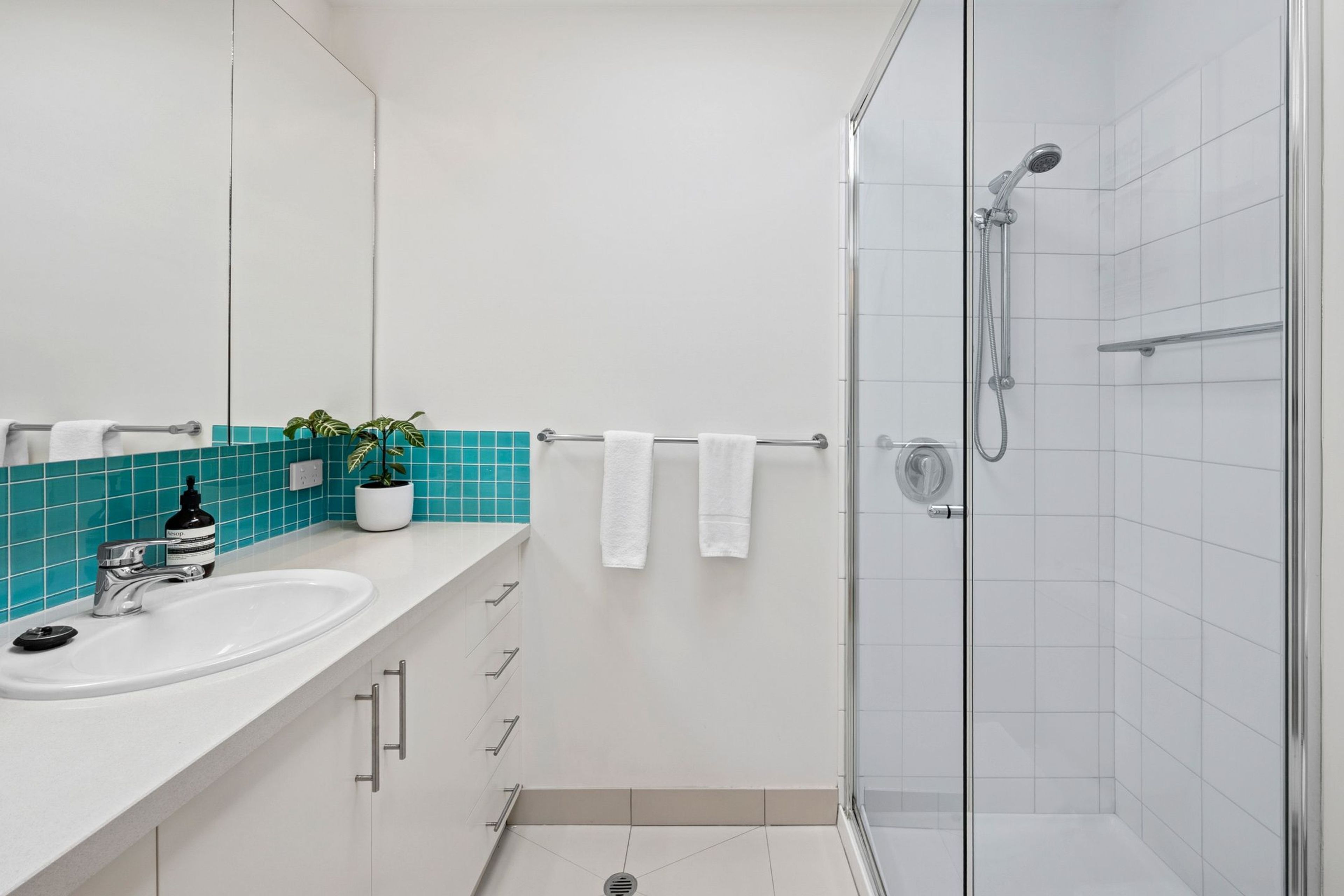 Ein modernes Badezimmer mit einer Duschkabine aus Glas, einem weißen Waschbecken und einem Spiegel.