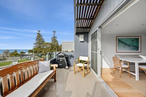 Ein Balkon mit Holzbank, Grill und Tisch mit Stühlen.