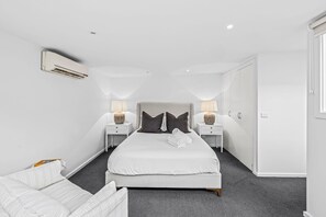 Ein modernes Hotelzimmer mit einem großen Bett, zwei Nachttischen mit Lampen, einem Kleiderschrank und einer Klimaanlage.