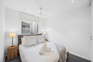 A hotel room with a bed, two bedside lamps, a ceiling fan, a window with a view, and a mirror on the wall. - Oceanview on Mountjoy (Lorne)