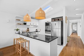 A modern kitchen with a central island, stainless steel appliances, and wicker pendant lighting. - Oceanview on Mountjoy (Lorne)