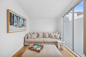 A modern living room with a beige sofa, a small side table, and a large window. - Oceanview on Mountjoy (Lorne)