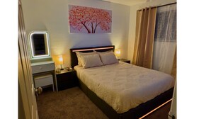 Un dormitorio ordenado con cama, mesitas de noche, una lámpara de pared y ventana con vistas al exterior.
