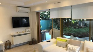 Una sala moderna con un sofá blanco, un televisor de pantalla plana montado en la pared y un amplio ventanal corredizo que da a un espacio exterior.